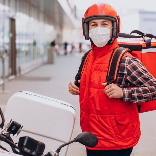 Food delivery boy driving scooter with box with food and wearing mask Food delivery boy driving scooter with box with food and wearing mask